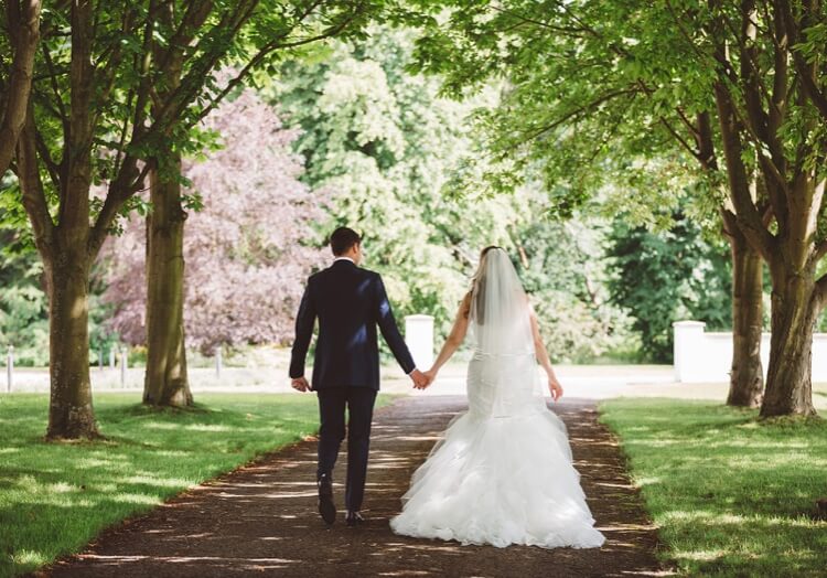 Bride & Groom walking down a tree lined avenue at Swynford Manor