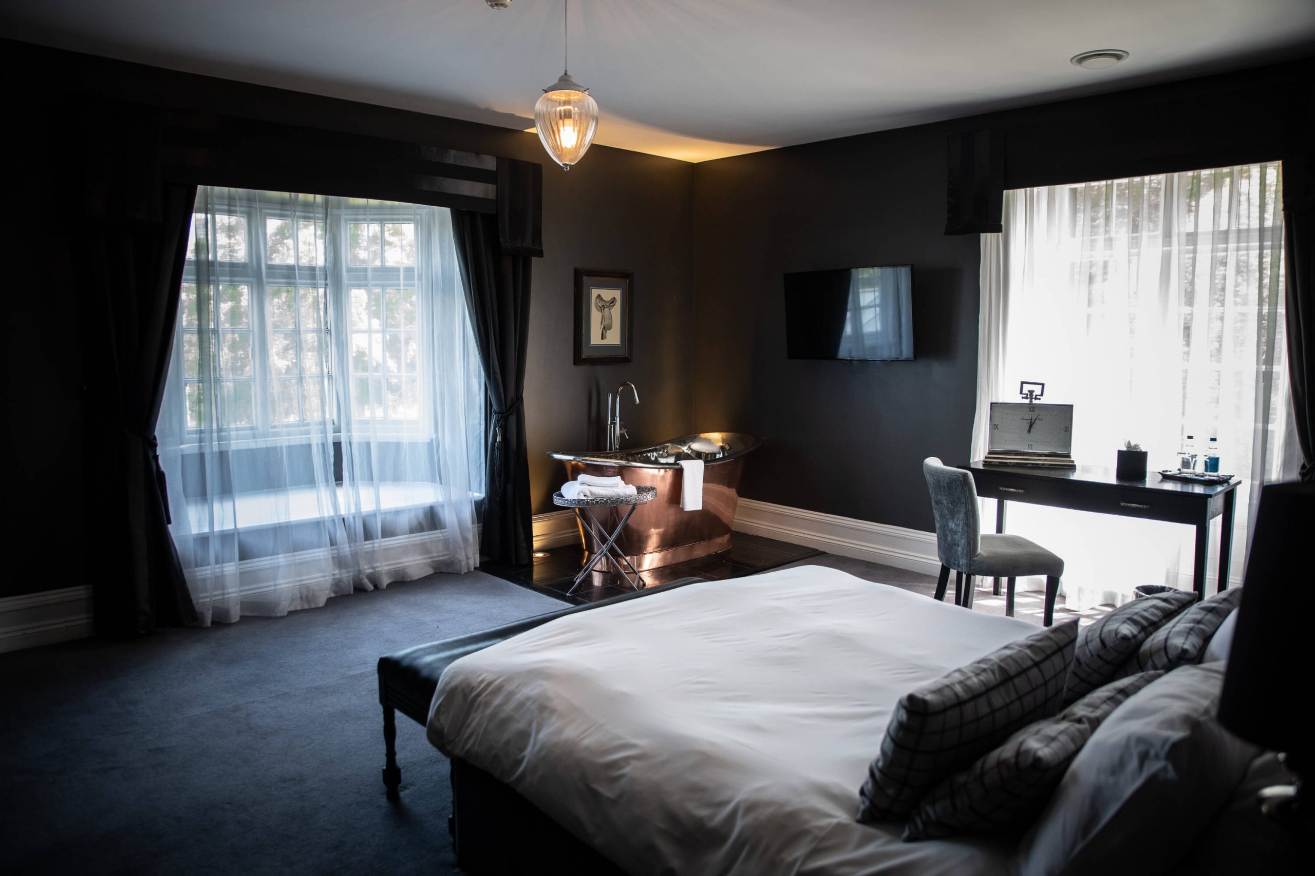 Guest room at Swynford Manor with monochrome decor showing copper roll top bath and teo windows overlooking the gardens