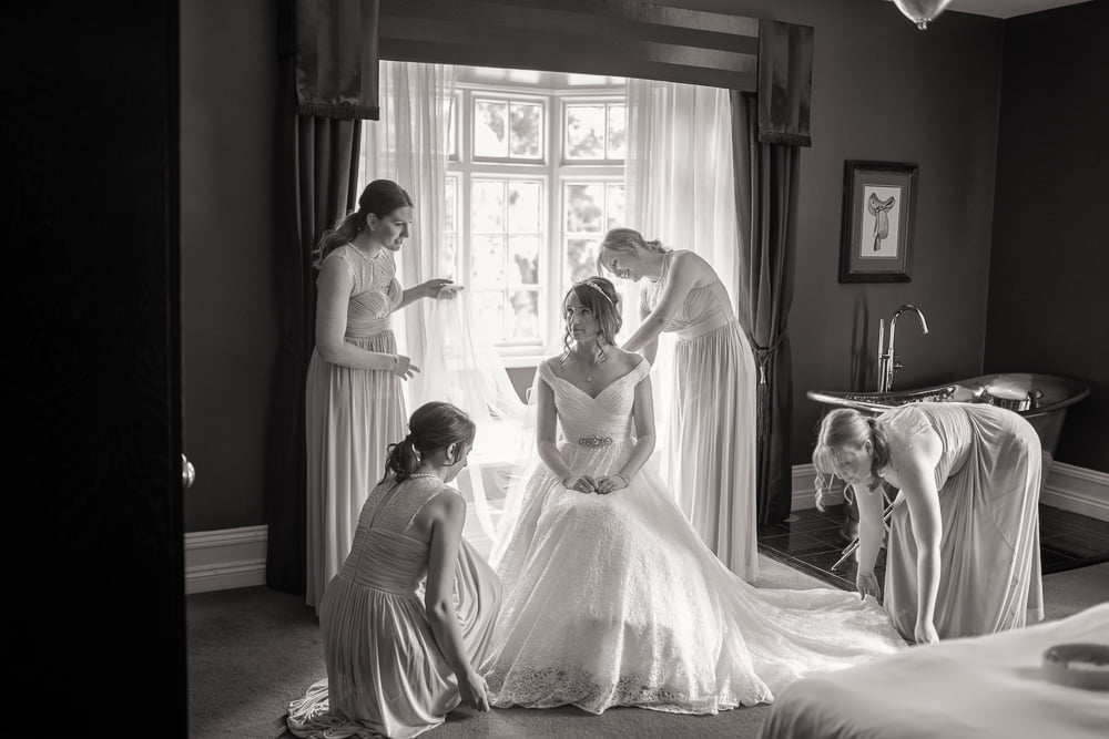 Black and white image of bride being attended by her bridesmaids in the bridal suite at Swynford Manor