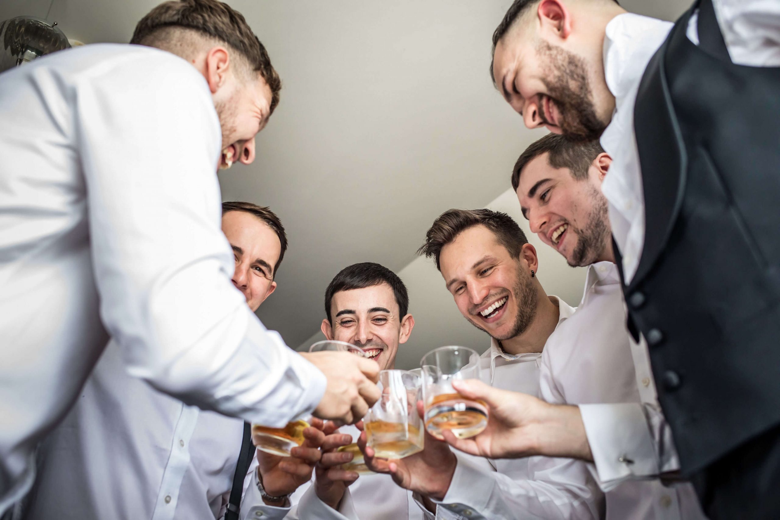 Groom and his groomsmen clinking glasses as they take a quick drink while gretting ready for the wedding ceremony at Swynforf Manor
